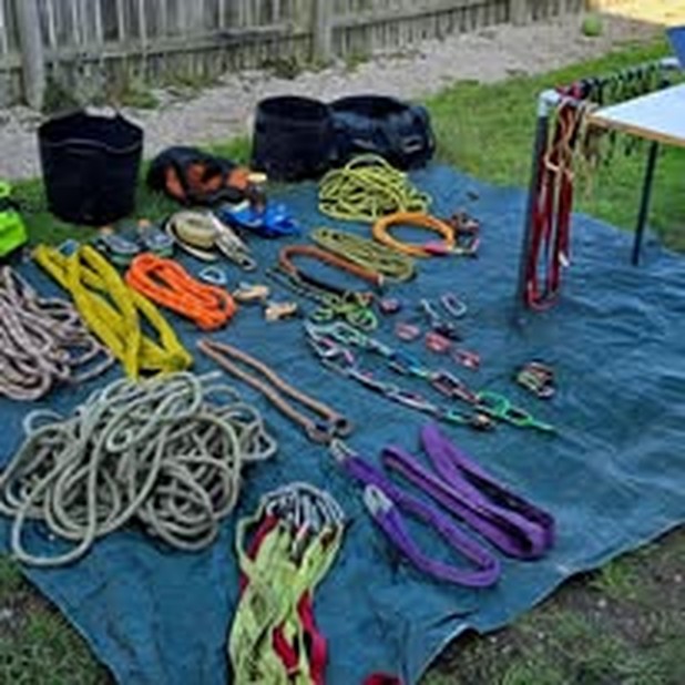 A large set of climbing and rigging equipment, including ropes, round slings and karabiners, laid out on a tarpaulin outdoors